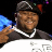 Pixelated static image of a person wearing a dark cap, silver chain necklace, and dark shirt with white trim against a black background.
