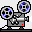 Pixelated film projector with two reels, gray body, white stripe, red dot on base, blue and black reel patterns against light background.