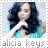 Alicia Keys in a turquoise top with long dark hair, forming a heart shape with hands, text below changes from gray to red.