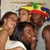 Four people in a group pose with one person wearing a colorful Rastafarian-style hat featuring green, yellow, and red stripes.