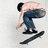 Pixelated figure in dark cap and blue pants bends over holding a long dark object against light gray background.