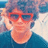 Pixelated image of a person with light skin wearing red sunglasses and a dark blue top against a blurred background.