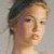 Pixelated close-up of a person's face with light brown hair, visible nose and mouth, against a neutral gray background.