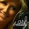 A close-up of a smiling person with light brown hair, wearing a dark top with white text reading 'ash beauty' in a stylized font.