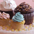 Pixelated image of three cupcakes with different frostings on a light background, next to blue text reading "Cute as a Cupcake" on pink.