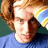 Pixelated image of a person with light brown hair wearing blue shirt and striped headband, set against green background with pixelated text.