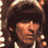 Pixelated static image of a person with dark hair and light skin tones, wearing a white shirt against a brown background with pixelated highlights.
