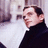 Pixelated static image of a person with dark hair wearing a black turtleneck sweater against a light background with blurred shapes.