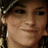 Pixelated close-up of a person's face with dark hair, brown eyes, and light skin showing a slight smile against a dark background.