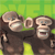 Two cartoon monkeys with brown fur and light faces stand side-by-side against a green grid background, both smiling with open mouths.