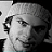 A black-and-white image of a person wearing headphones and a beanie, with red text overlays changing across frames.