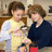 Two people in a kitchen setting with one holding an object, surrounded by pink background and pixelated text.