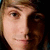 Pixelated close-up of a person's face with light brown hair, showing one eye and part of the nose against a dark background.