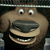 Pixelated cartoon dog face with large round eyes, wide open mouth showing teeth, and a dark nose, set against a dark background with horizontal light strip.
