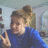 A pixelated image shows a person with light brown hair wearing a blue top, making a peace sign with their right hand against a blurred background.