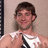 A pixelated image shows a person in a white sleeveless shirt with dark straps, standing against a light brown background next to pink text reading "John + Valentina" on a light blue field.