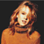 A pixelated portrait of a person with light brown hair wearing an orange top against a dark background.