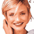 Pixelated static image of a smiling person with light brown hair, hand near face, wearing dark clothing against white background.
