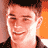 Static pixelated image of a person's face with short dark hair, wearing a dark jacket over light clothing against an orange and brown background.