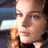 A pixelated image of a woman with light brown hair and blue eyes, wearing a blue top with a red and yellow Superman logo on it.