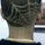 A person's head and neck viewed from behind, showing a patterned haircut with curved lines on the scalp, wearing a dark shirt with a light collar.