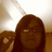 Pixelated static image of a person with long brown hair and glasses, holding an object near their face against a light background.