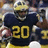 Pixelated image of a football player in a dark blue jersey with yellow number 20, wearing a yellow helmet and dark face mask, holding a football.