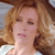 A pixelated close-up of a person with light brown curly hair, closed eyes, and a neutral expression, wearing a white top against a blurred background.
