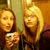 Two women in a mirror selfie, one holding a silver camera, with visible background elements.