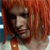 A pixelated close-up of a person with reddish-brown hair, dark eyes, and a neutral expression, set against a blurred background with warm tones.