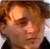 Pixelated close-up of a person's face with light brown hair, wearing dark clothing, against a blurred background.