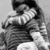 Pixelated grayscale image of two figures in close embrace, one figure with dark hair and light clothing, the other with lighter hair and darker clothing, against a plain background.
