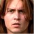 Pixelated close-up of a person's face with light brown hair, neutral expression, and visible eyes, nose, and mouth against a dark background.