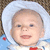 A baby in a white bonnet and blue-and-white outfit with red accents smiles against a brown textured background.