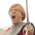 Pixelated image of a person with light brown hair shouting, wearing a gray shirt with red accents and holding a dark object.