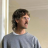 Pixelated image of a person with dark hair wearing a gray shirt, positioned against a light-colored wall with a vertical white stripe on the left.