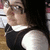 Pixelated static image of a person with dark hair wearing a black top with white collar, set against a blurred background with brown and white tones.