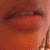A pixelated close-up of a reddish-brown face with dark eyes and lips, set against a gradient background transitioning from deep red to light pink.