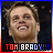 Pixelated close-up of a smiling person with light brown hair against dark background, text "TOM BRADY!!!" in red and blue at bottom.