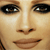 A pixelated close-up of a person's face showing eyes, nose, and mouth with a neutral expression, rendered in warm brown and beige tones.