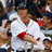 A pixelated image of a baseball player in white uniform with red accents, standing among other players on a field.