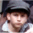 Pixelated close-up of a person wearing a dark cap and light-colored shirt, with visible ear and partial facial features.