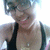 A person wearing a black tank top and glasses smiles broadly in a bright, overexposed setting with visible pixelation.
