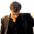 Static pixelated image of a person with short brown hair wearing a black shirt, viewed from the shoulders up against a white background.