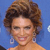 Static pixelated image of a woman with curly brown hair, wearing large silver earrings and an orange dress against a blue background.