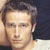Static pixelated portrait of a person with short dark hair and light skin, cropped to show upper face and shoulders against a gradient background.