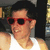 Pixelated image of a person wearing red sunglasses and a white shirt, with dark hair against a blurred background.