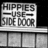 Pixelated grayscale image showing a sign with text 'HIPPIES USE SIDE DOOR' on a building facade with a horizontal railing below.