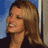Pixelated static image of a woman with long brown hair wearing a dark top against a blue background.