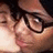 Pixelated close-up of a person with dark hair and glasses, showing partial facial features including eyes, nose, and mouth against a light background.